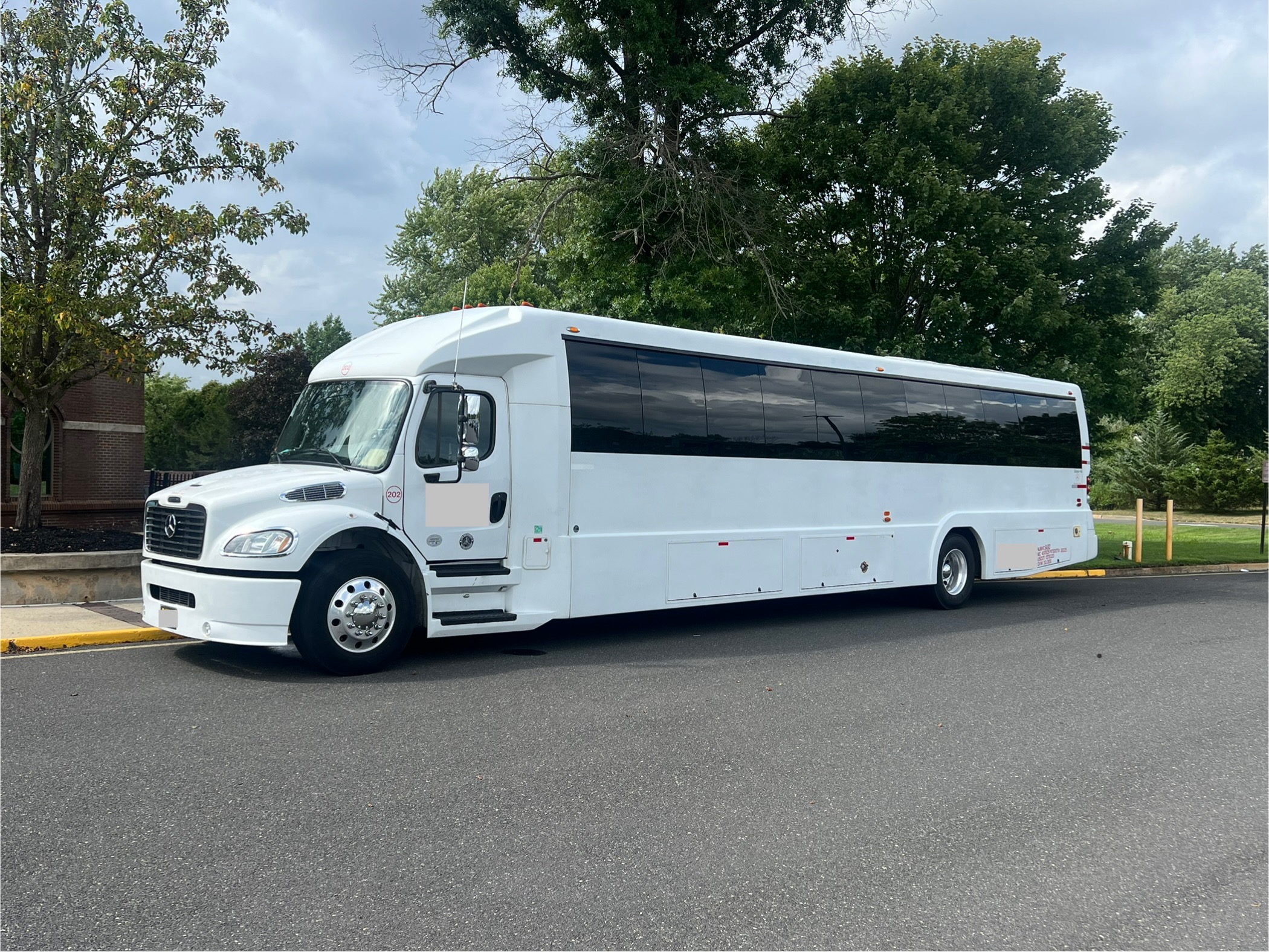 A white luxury coach bus parked on a paved road with trees in the background.