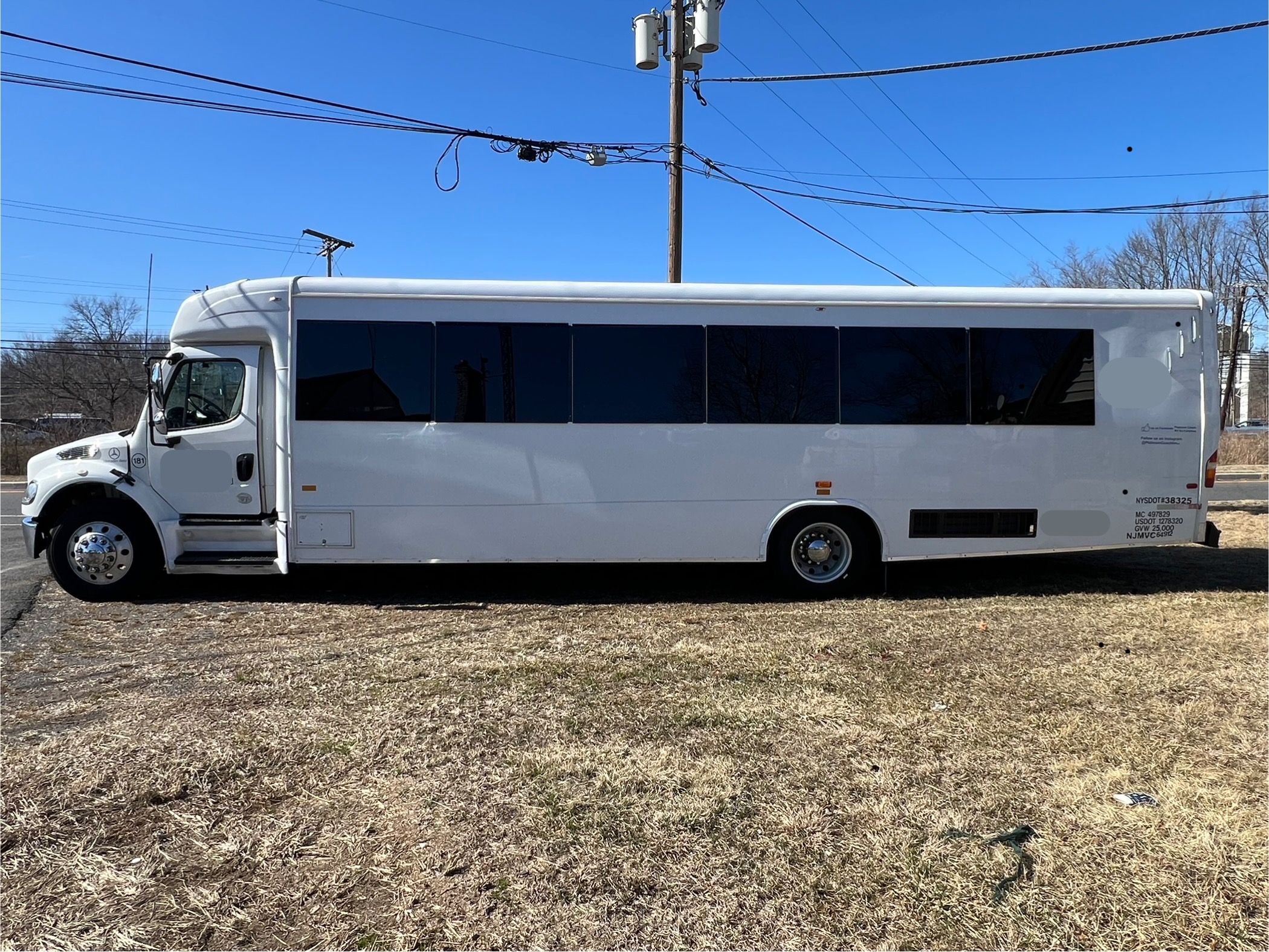 White shuttle bus with tinted windows parked on grass under a clear blue sky.