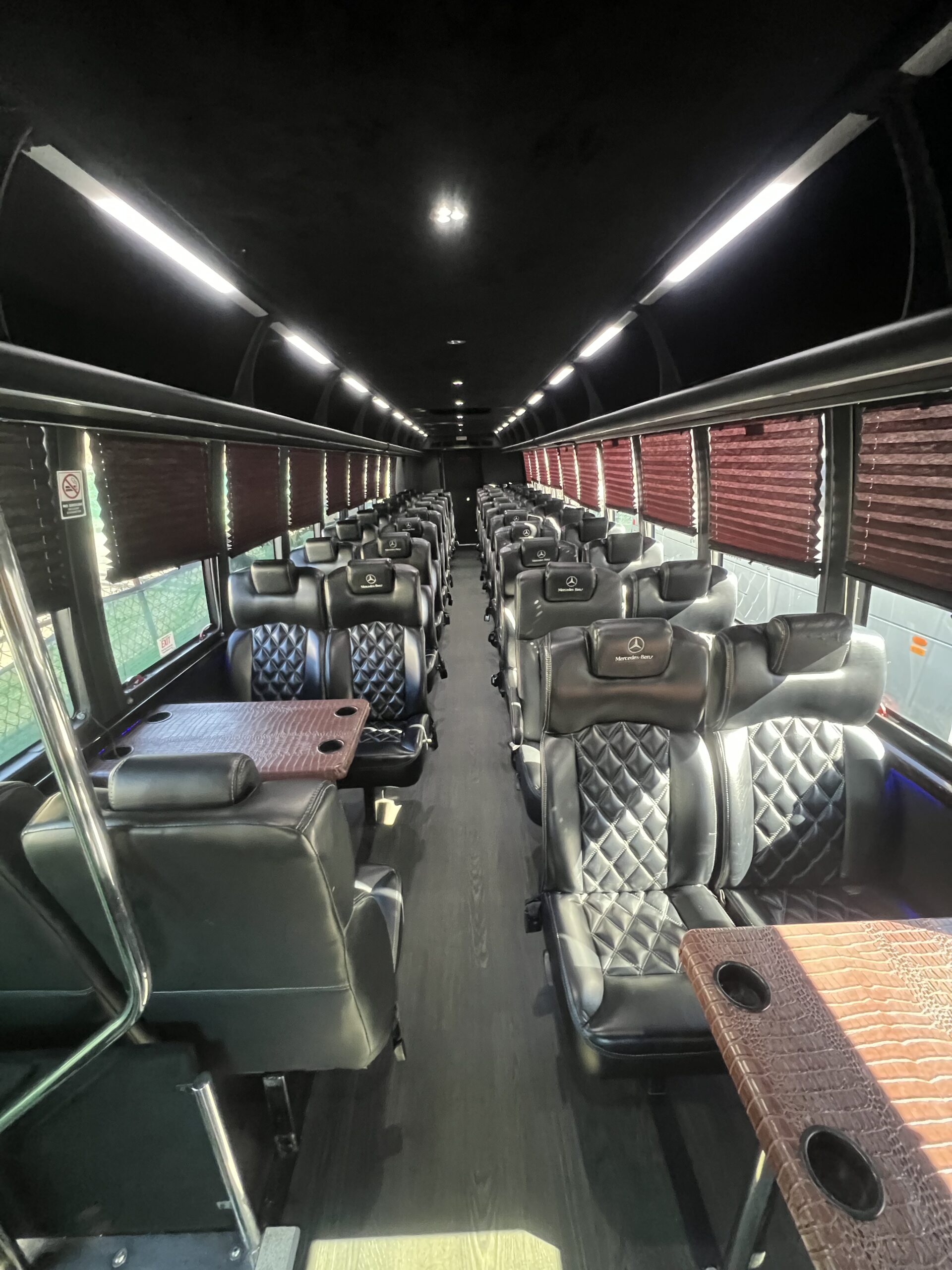 interior view of a luxury bus, showing black leather seats, tables, and overhead lighting.