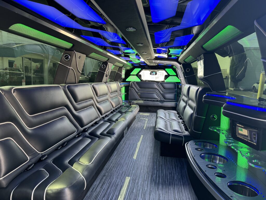Interior of a limousine with black leather seats, neon blue and green LED lighting, and a built-in bar area.