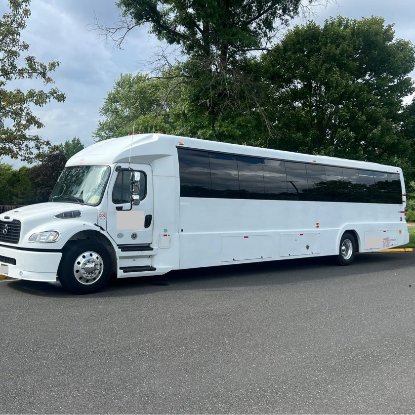A white luxury coach bus parked on a paved road with trees in the background.