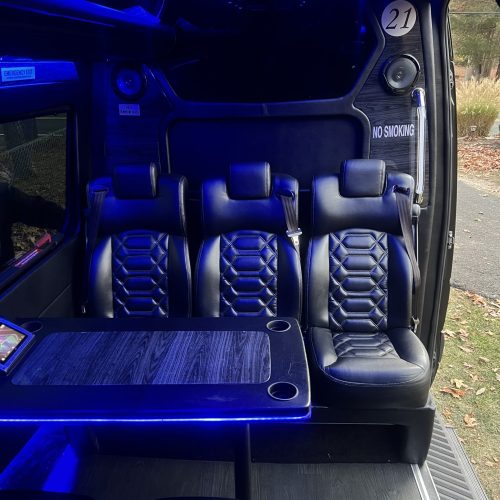 Rear-facing black leather seats inside a luxury van, lit with blue LEDs.